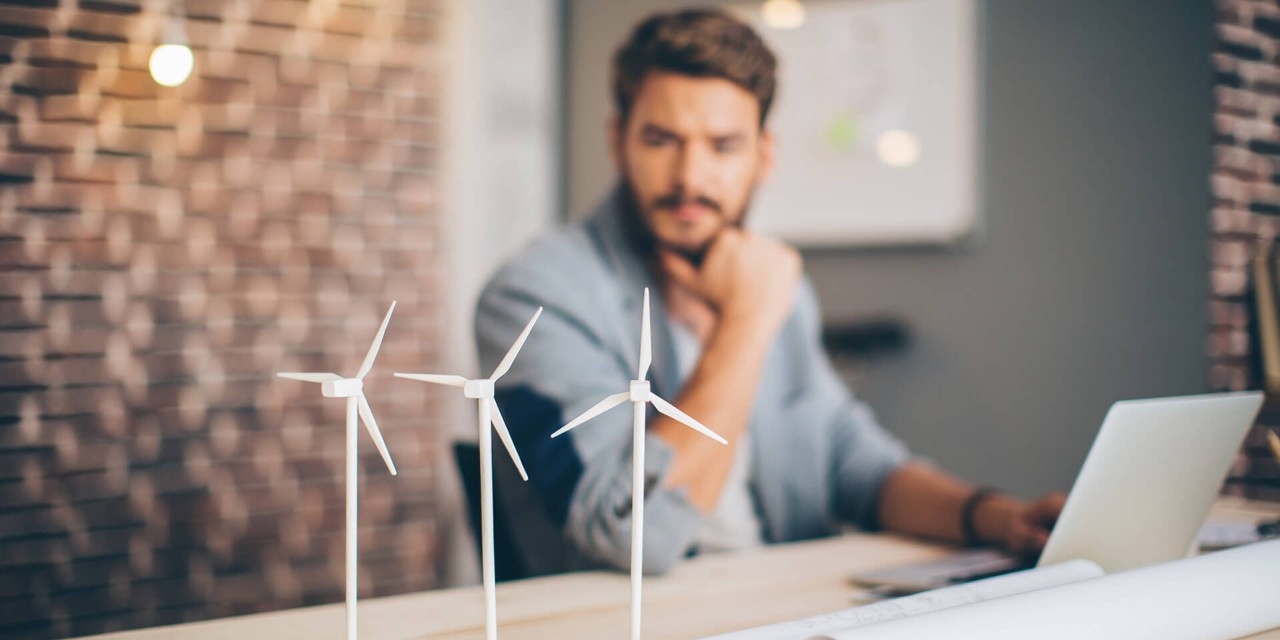 Windkraftradmodelle stehen auf einem Tisch, dahinter sitzt ein Mann und überlegt
