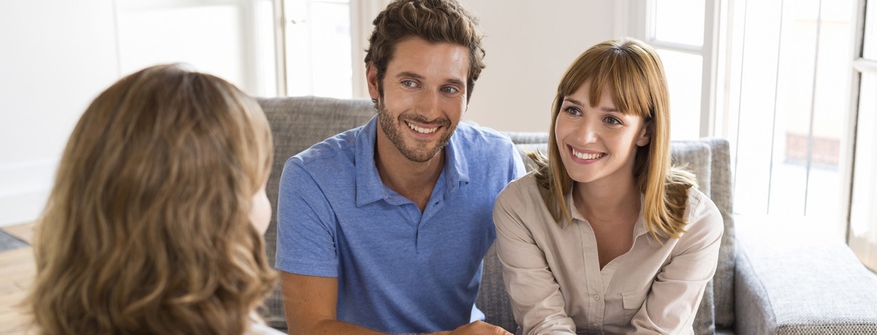 Mann und Frau sitzen auf einer Couch und unterhalten sich mit einer anderen Frau, welche gegenüber sitzt.
